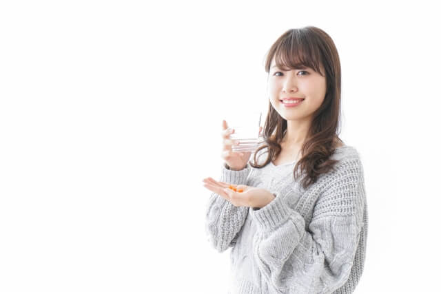 コップ１杯の多めの水でサプリを飲む女性